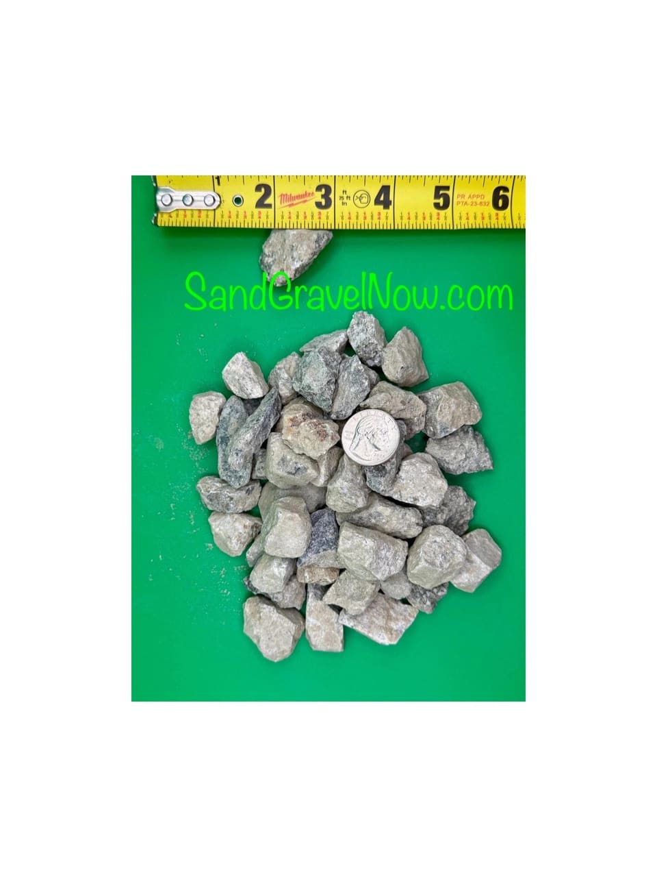 Gray 3/4 inch crushed rock pieces on a green board beside a quarter and a tape measure for scale.
