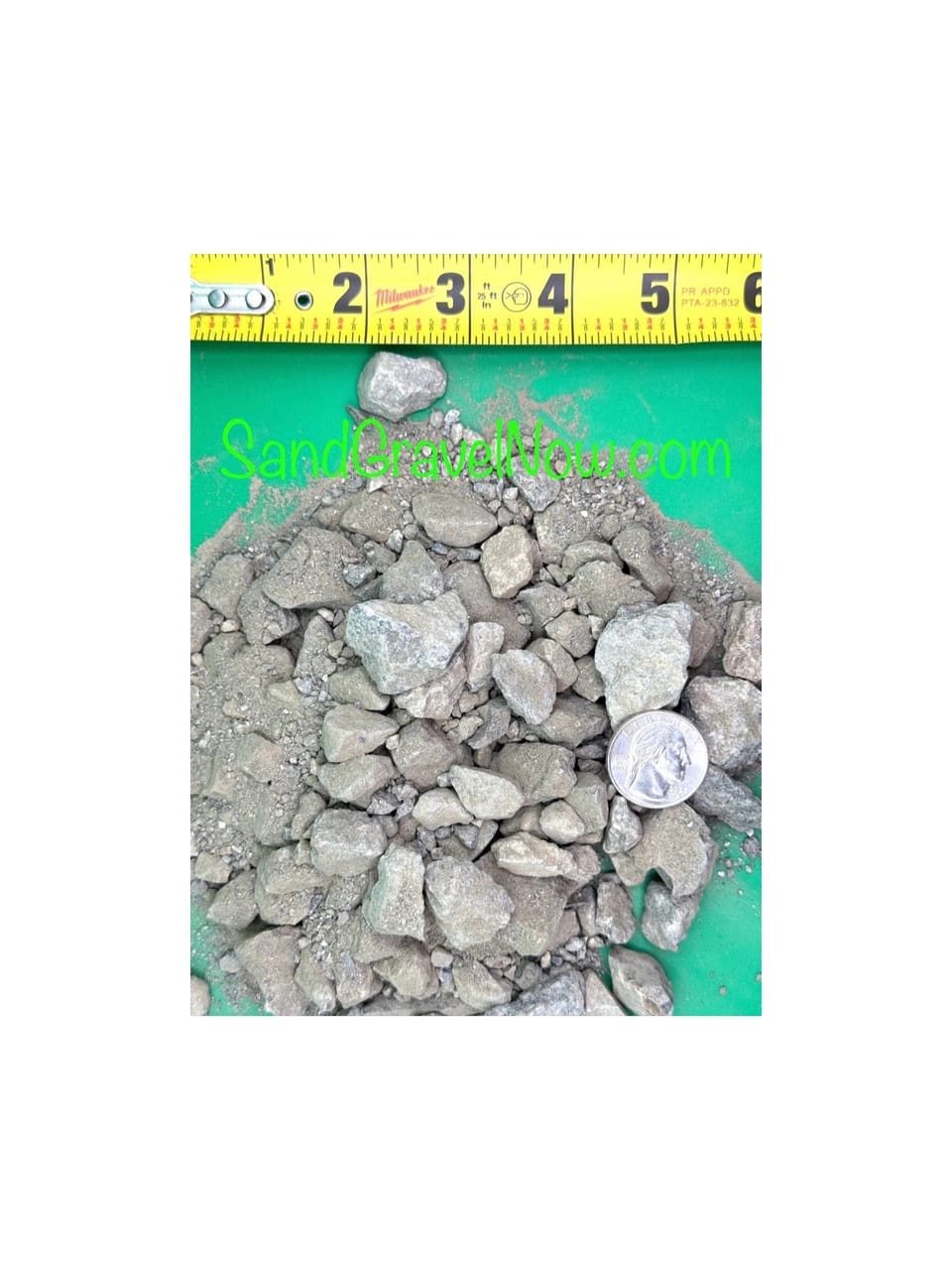 Gray angular 3/4 inch crushed aggregate base on a green board beside a tape measure and a quarter for scale.
