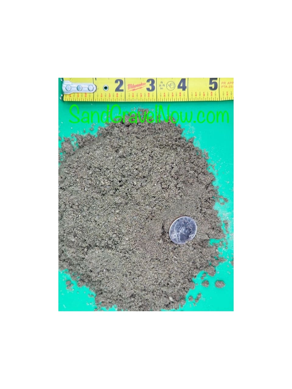 Pile of gray-brown fine sand on a green board beside a tape measure and a quarter for scale.